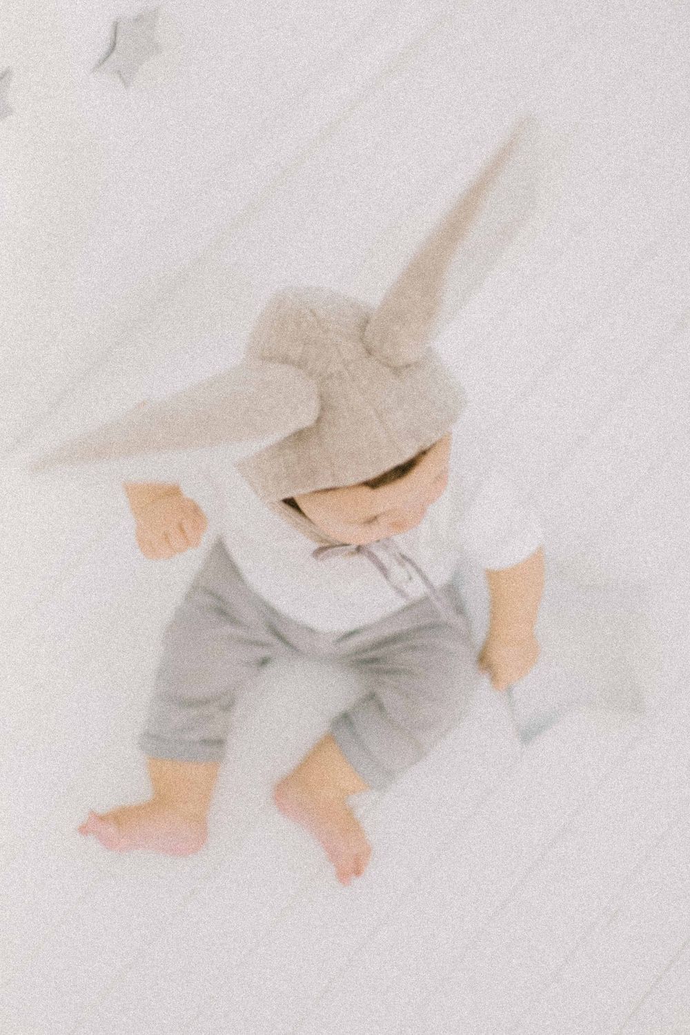 Minimalist images of a baby wearing grey bottoms crawling on white fabric. Estúdio de fotografia em Alenquer, Lisboa e Portugal.