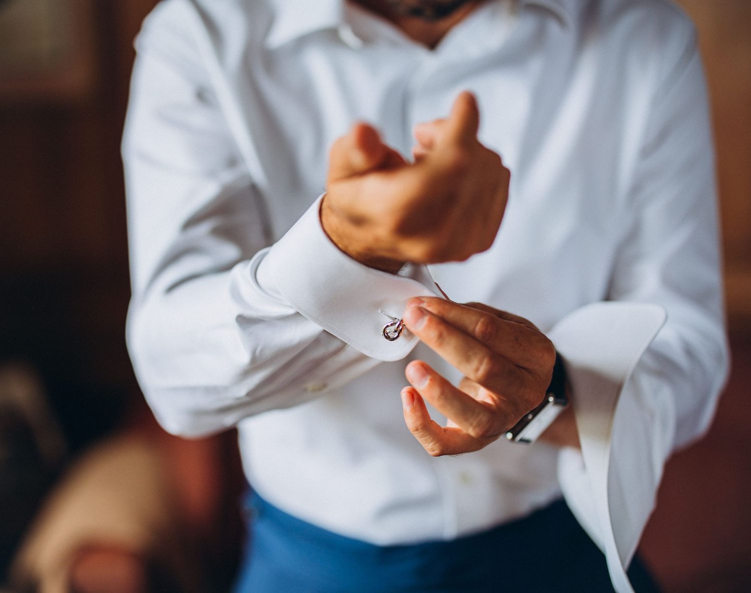 Close-up view of hands adjusting cufflinks on a crisp white dress shirt sleeve.