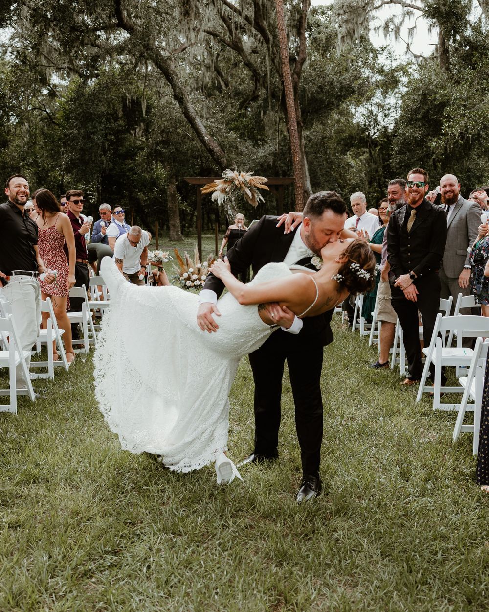 A sweet backyard wedding moment where couples and guests dance joyfully on a grassy lawn with white chairs.