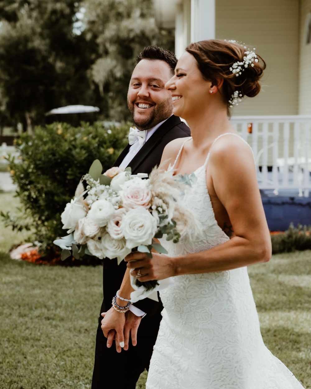 Bride and groom share candid laughs during outdoor wedding photoshoot with white bouquet and formal attire.