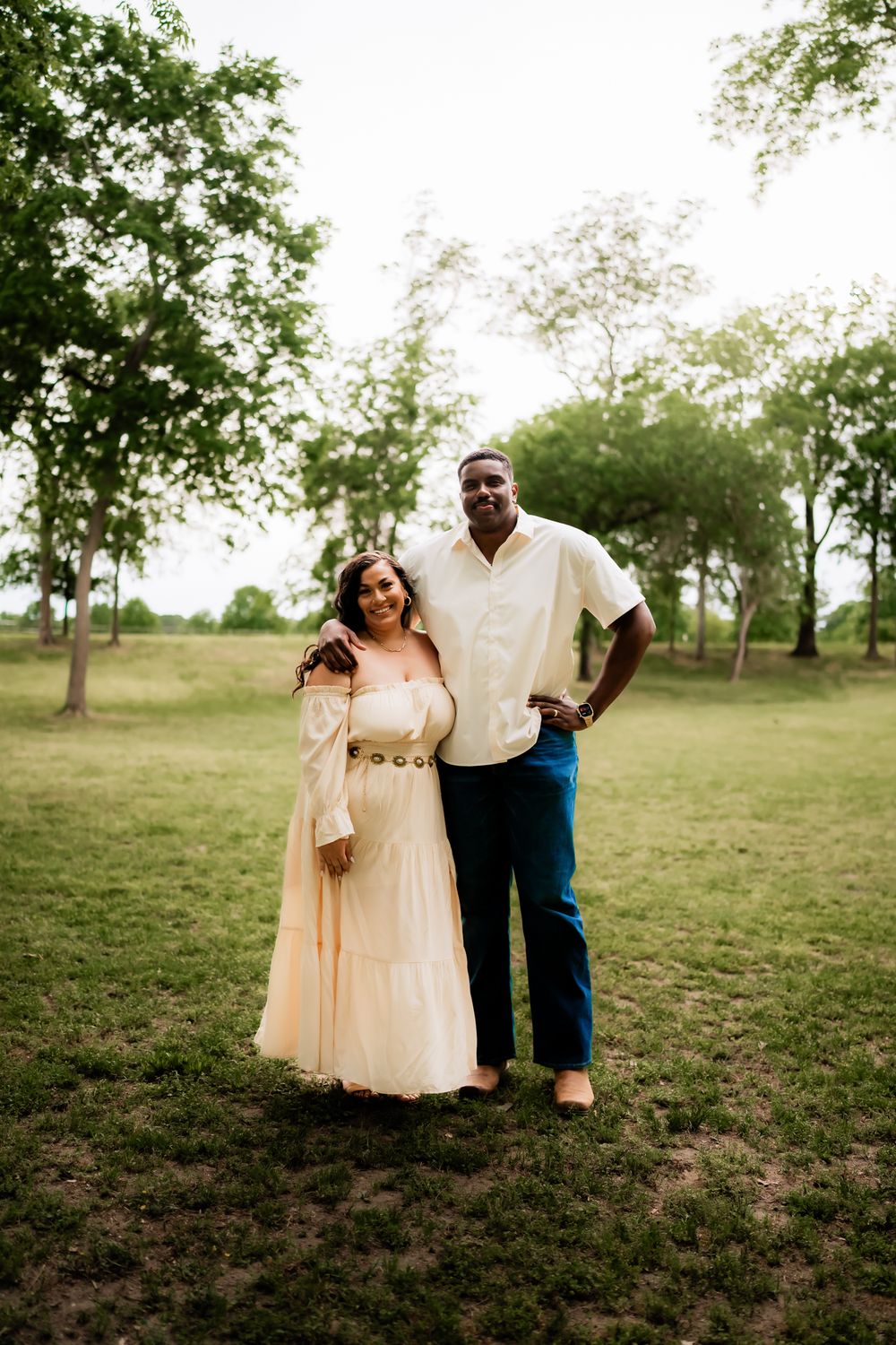 A couple shares intimate moments in a grassy field wearing light colored outfits during a romantic photoshoot.