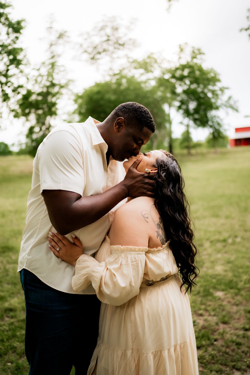 An intimate moment between a couple in light colored clothing as they share a tender kiss in a grassy field.
