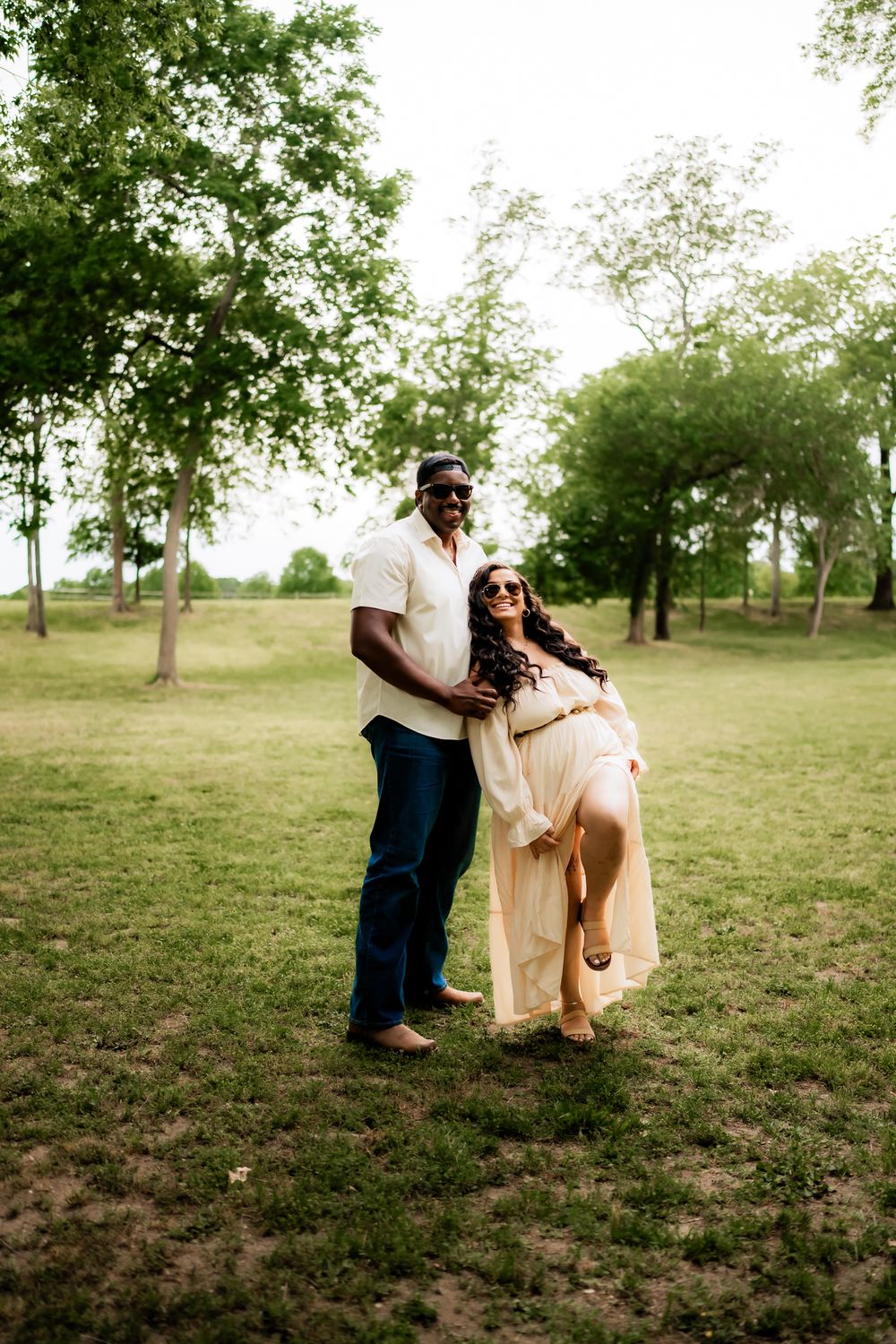 Romantic couple in light colored clothing poses playfully together in a sunlit outdoor setting.