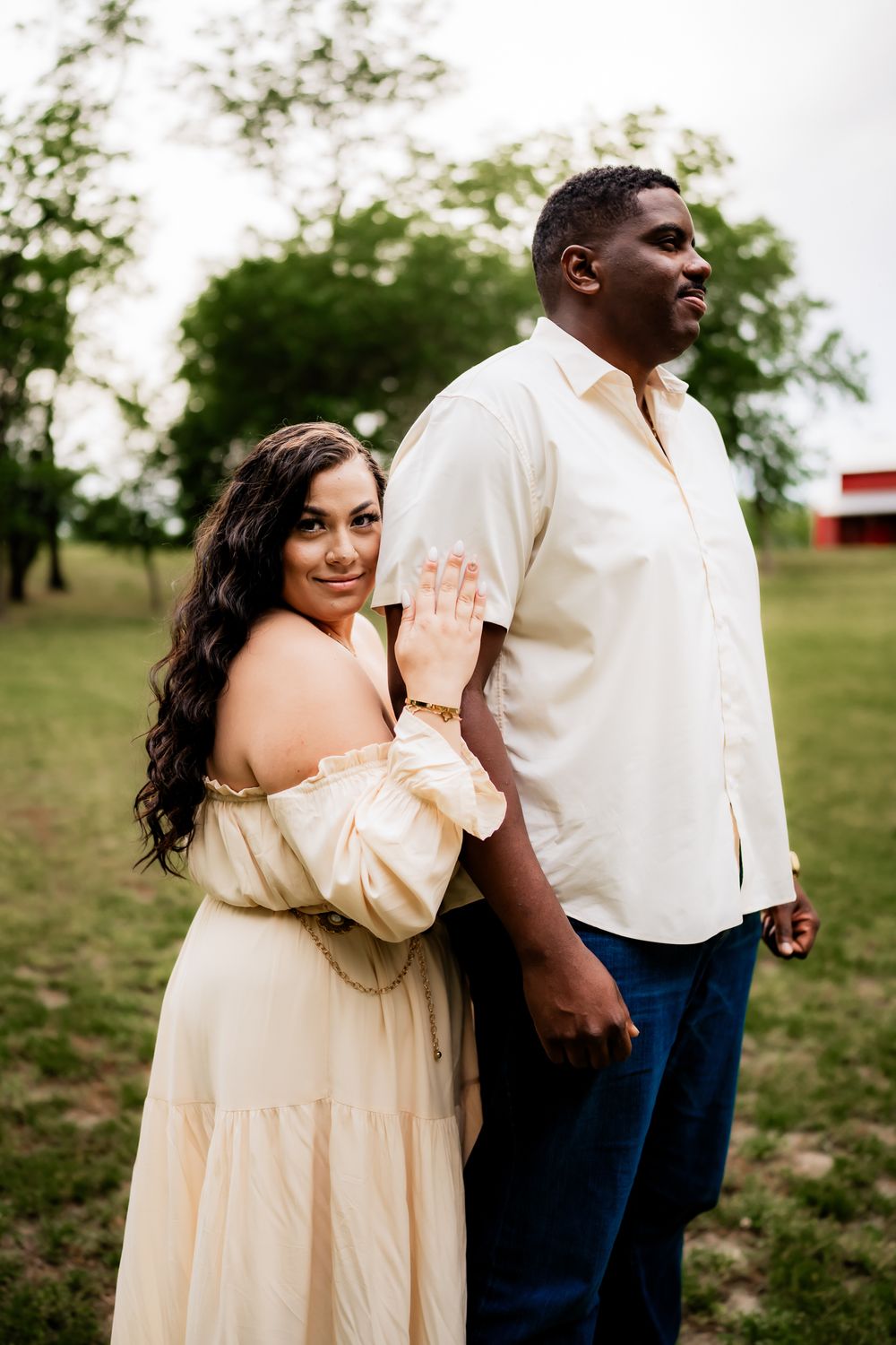 A couple in matching cream outfits share a playful moment while posing for photos in a grassy outdoor setting.