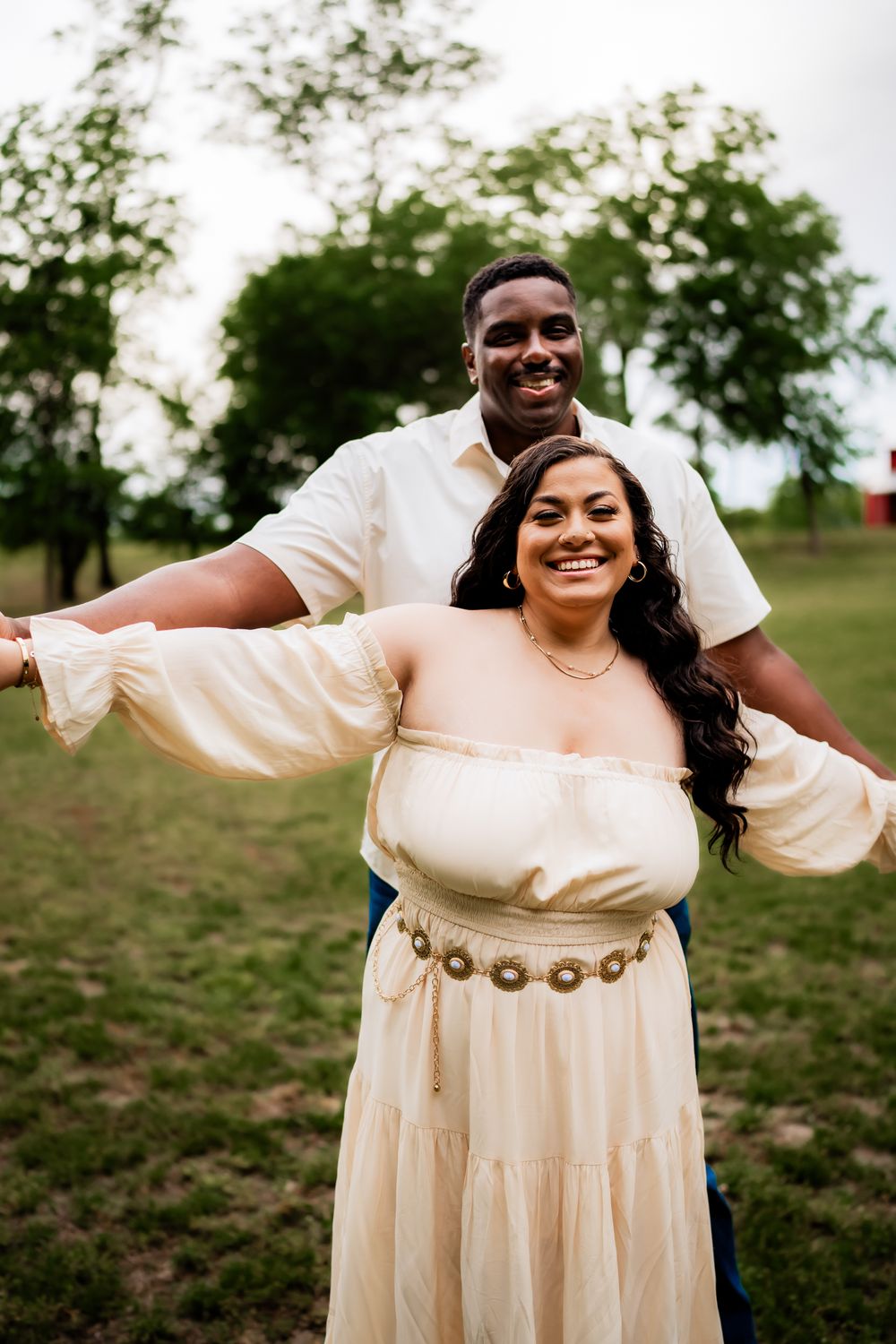 Joyful couple spreads their arms wide while posing together in a sunny outdoor setting.