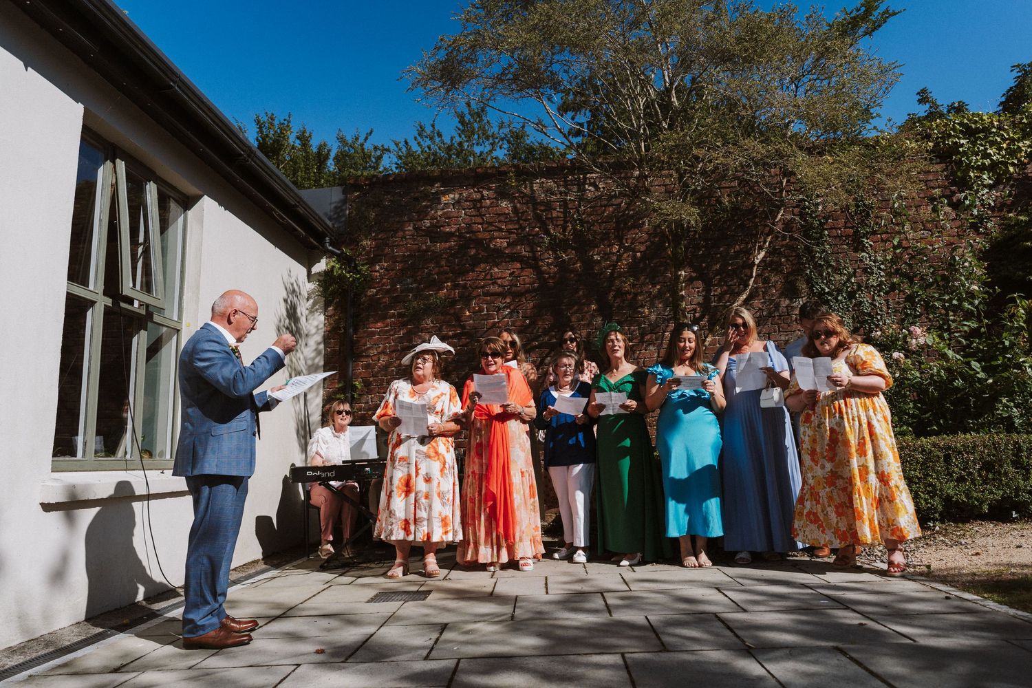 Wedding guests gather outside a white building on a sunny day during an outdoor celebration.