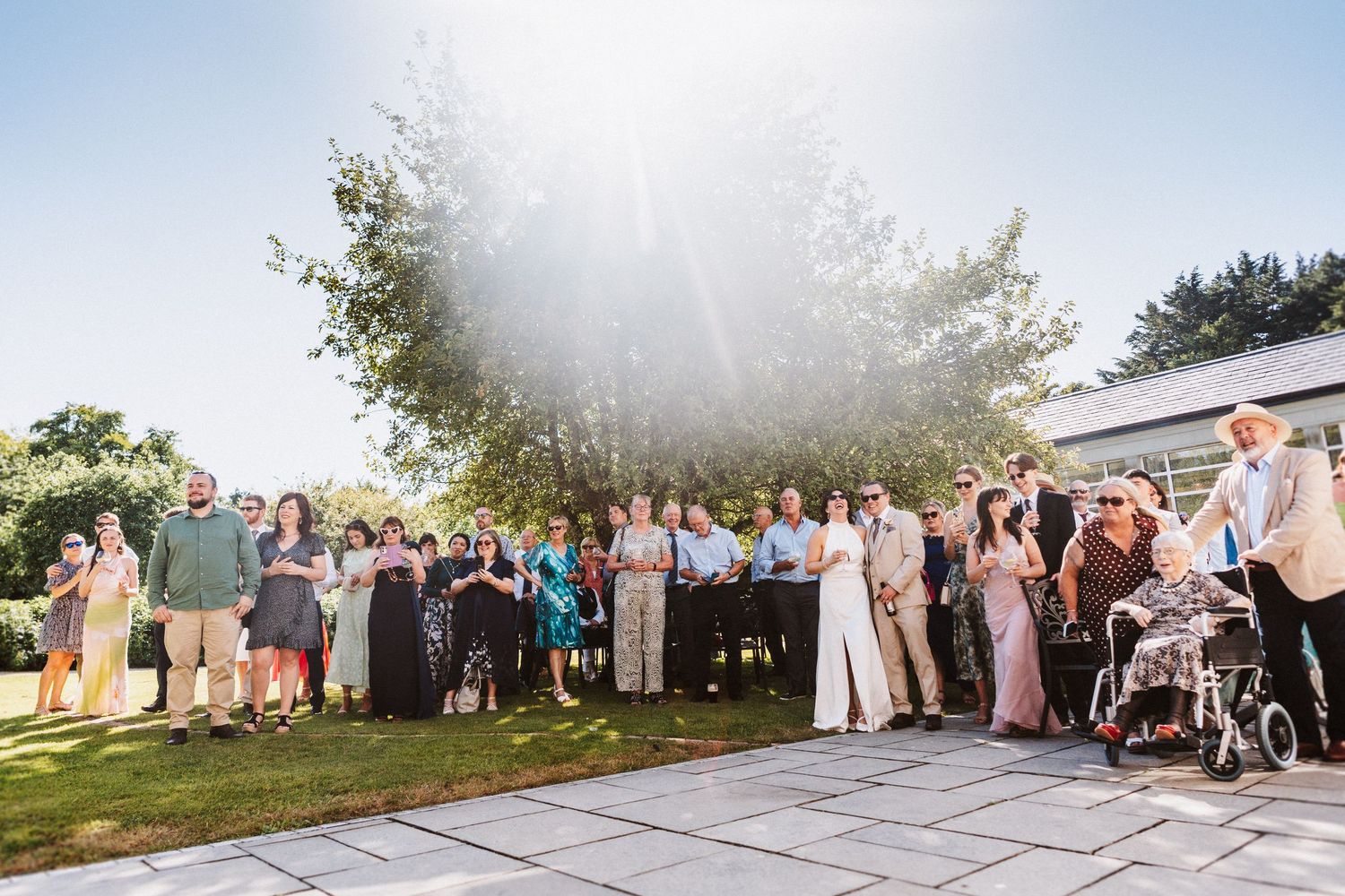 Wedding guests gather in a line outside during golden hour to celebrate the newlyweds at an outdoor reception.