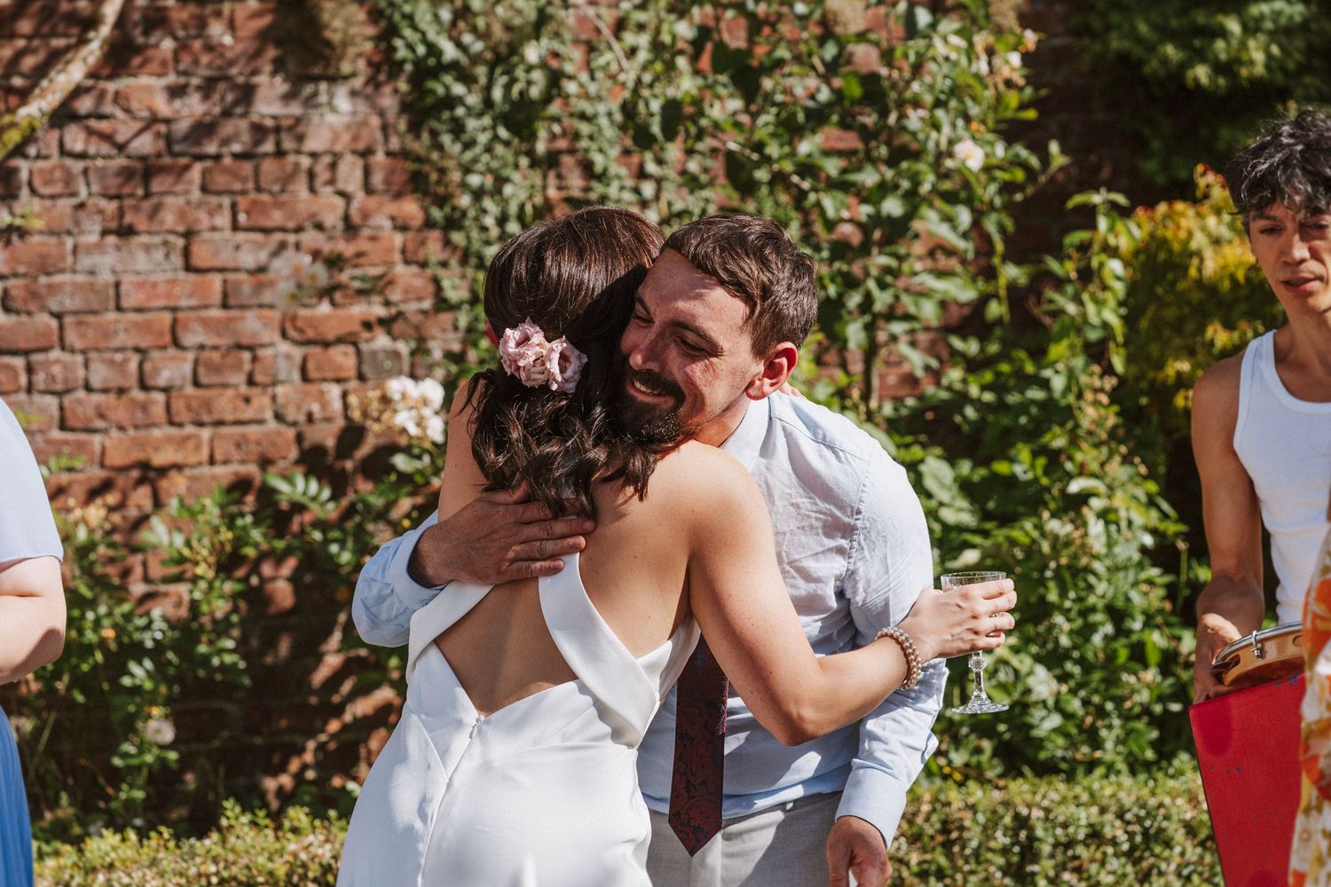 A couple in wedding attire dances and celebrates with joyful guests at an outdoor garden reception.