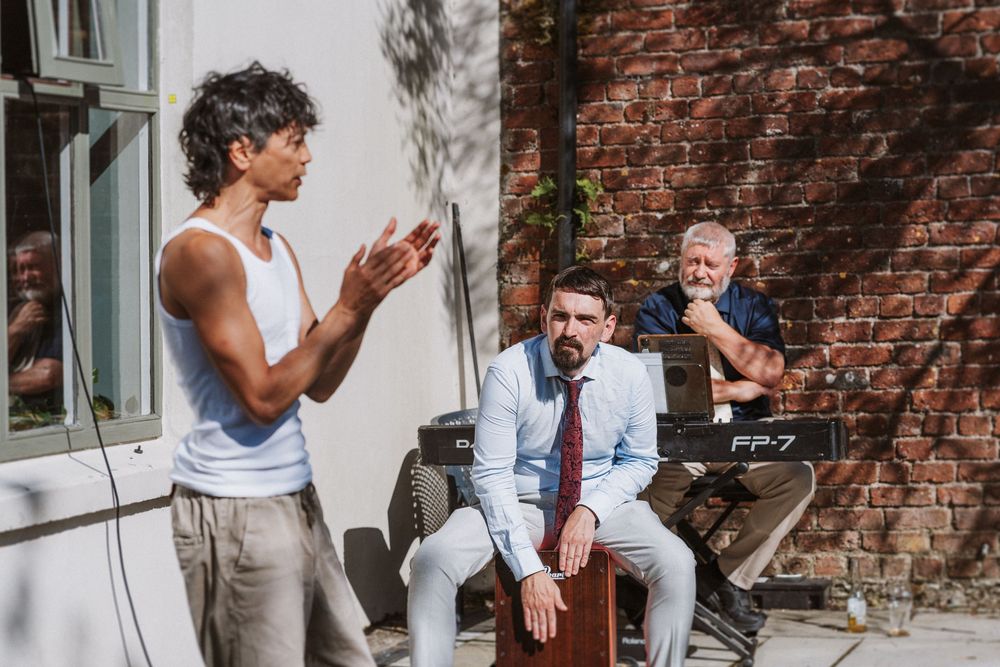 Group of people in formal attire having animated conversations near a brick wall exterior.