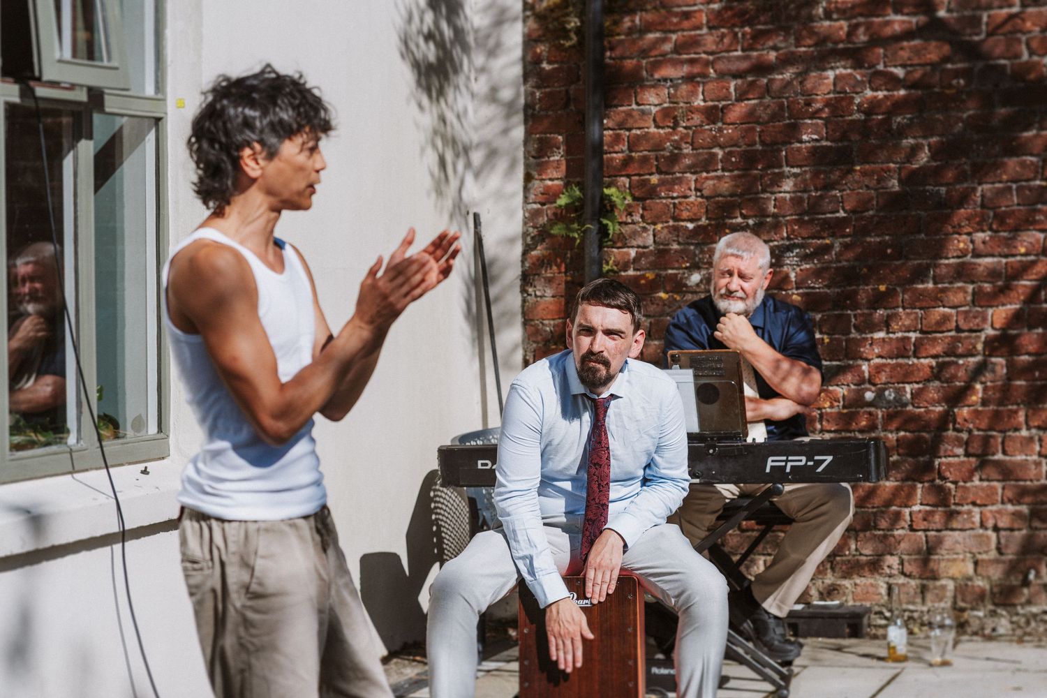 Group of people in formal attire having animated conversations near a brick wall exterior.
