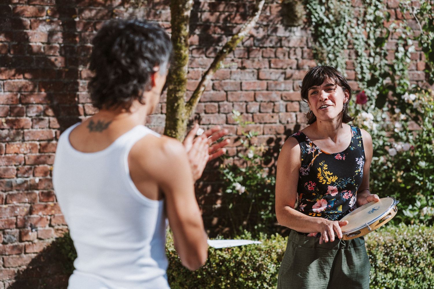 People gathered outdoors against a brick wall with greenery, engaged in casual conversation.