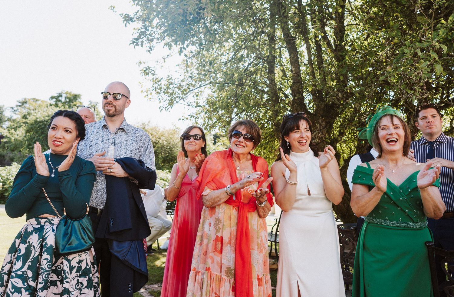 Wedding guests enjoy outdoor cocktail reception under trees during late afternoon celebration.