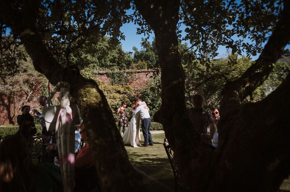 Guests gather outdoors under large shady trees during a summer celebration at a park.