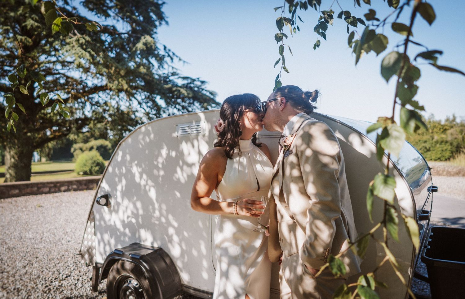A couple in a romantic outdoor photoshoot shares tender moments against a natural backdrop with sunlight filtering through trees.