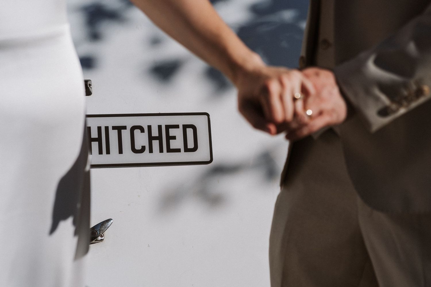 A couple holds hands next to a 'HITCHED' sign during their wedding celebration.