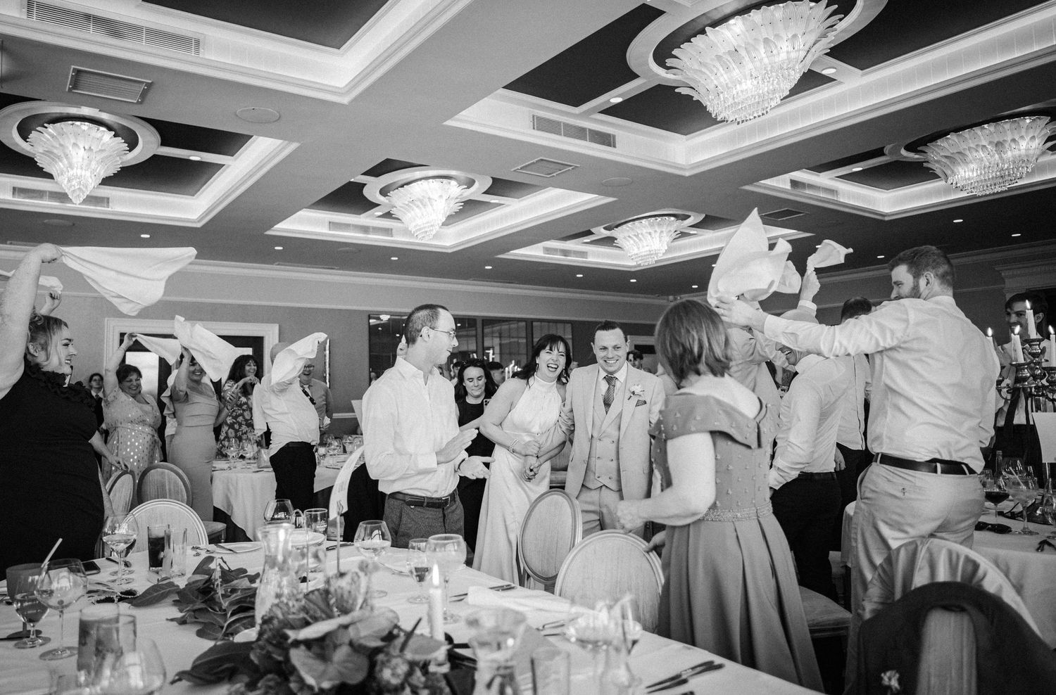 Black and white panoramic image of an elegant wedding reception party in a ballroom with crystal chandeliers.