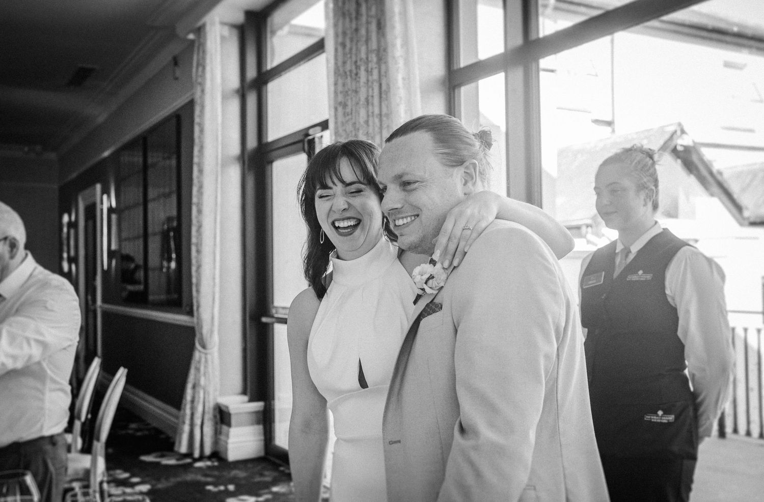 Happy couple share intimate candid moments during a wedding celebration at a bright indoor venue.