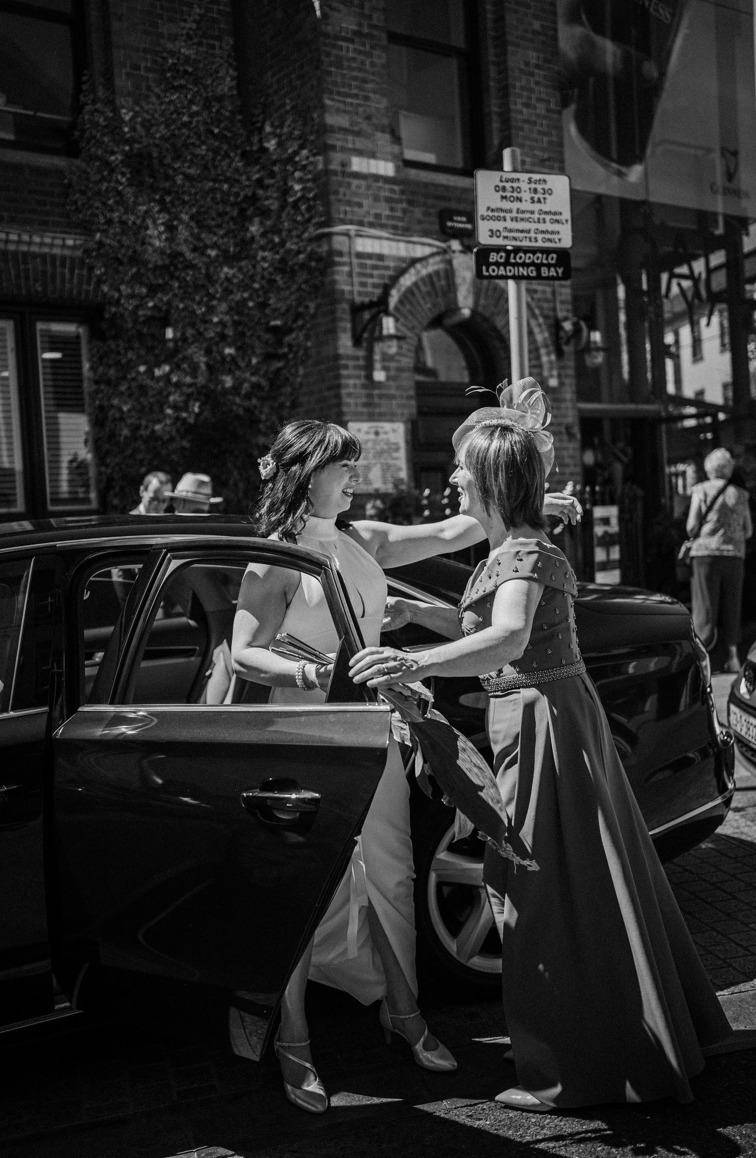 Two people provide car assistance in a dimly lit city street at night.