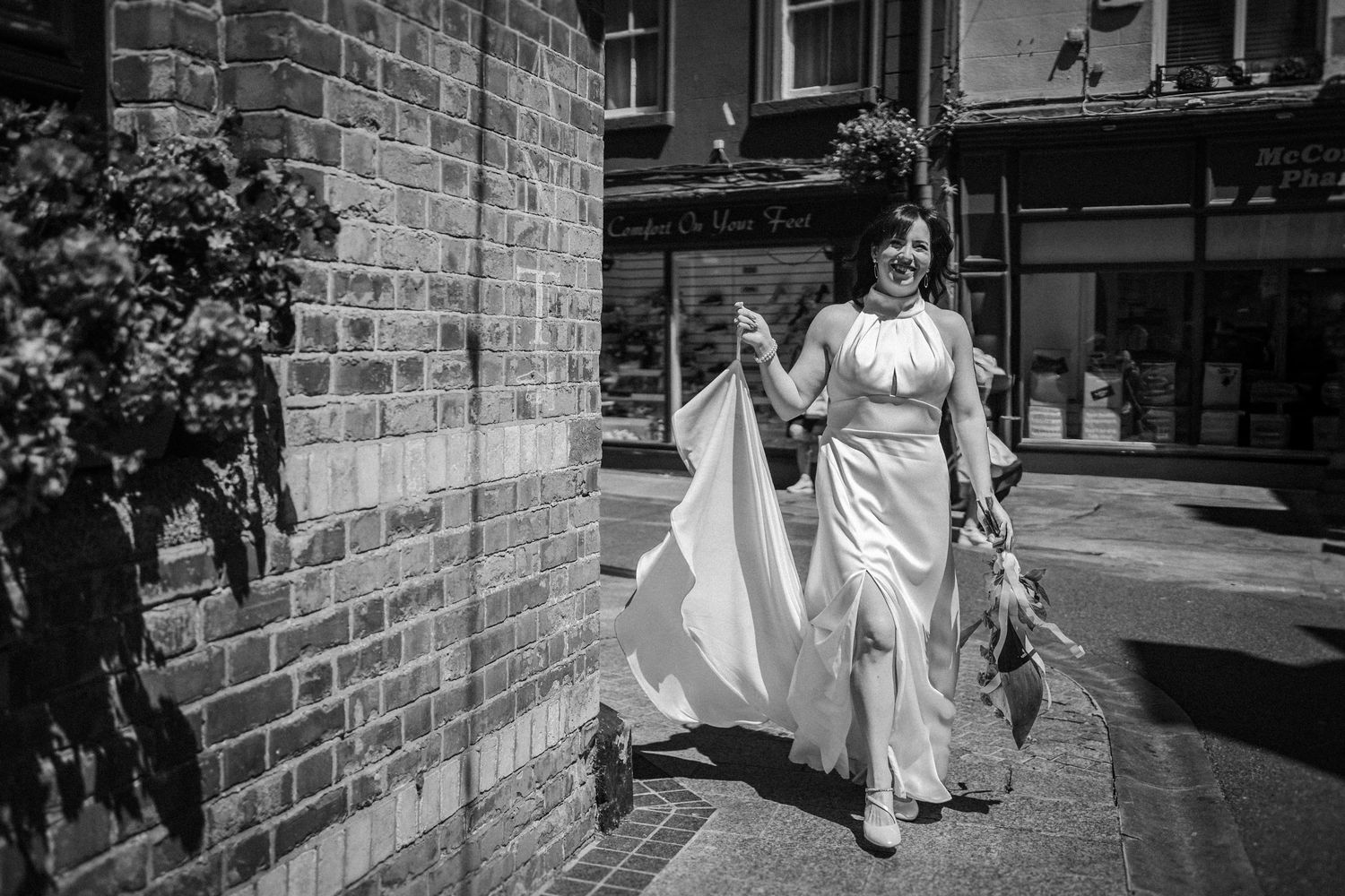 People in white wedding outfits walking on a brick-lined street in black and white photography.