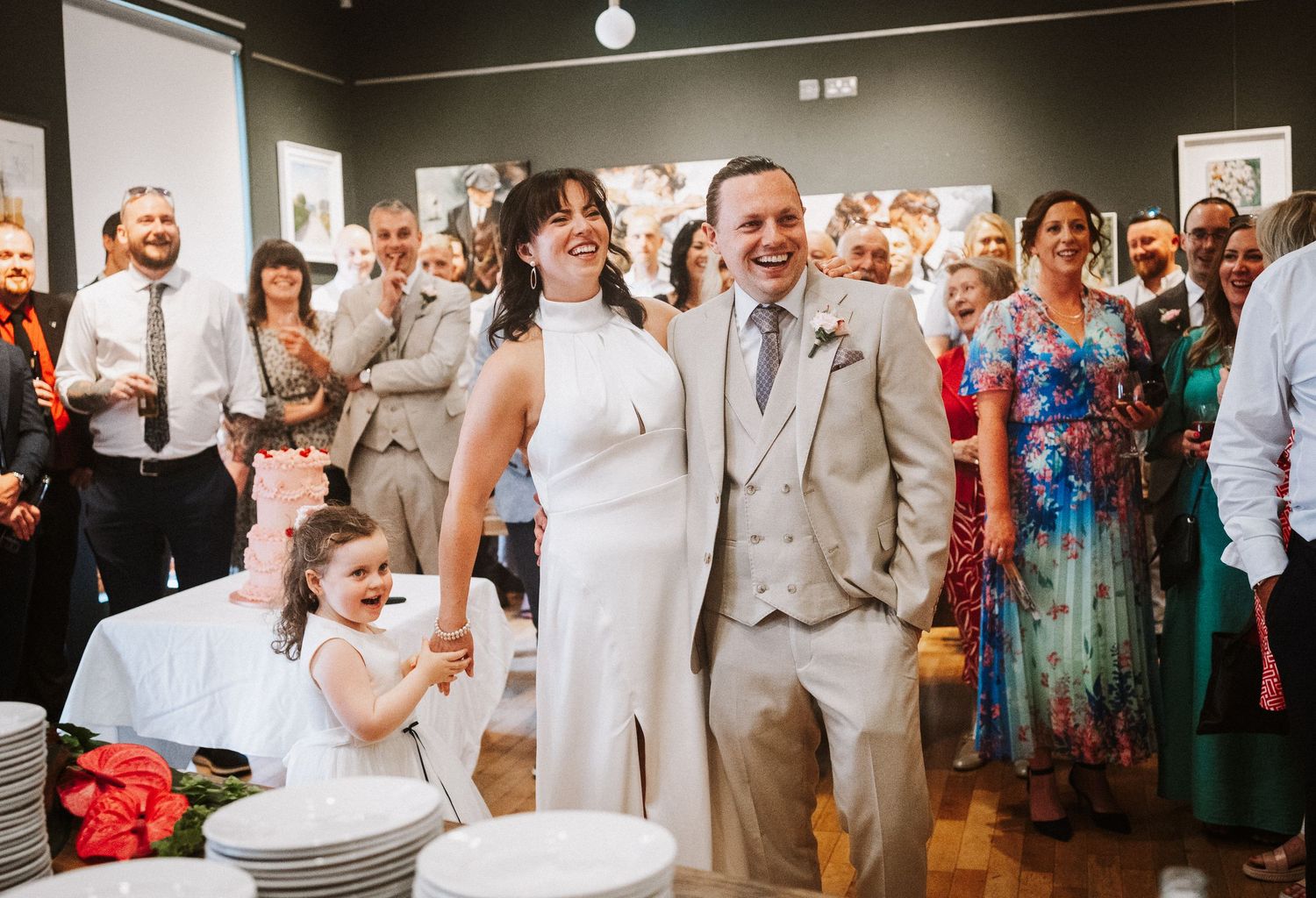 Wedding party and guests gathered tightly together in a row, celebrating in a rustic venue with wood floors.