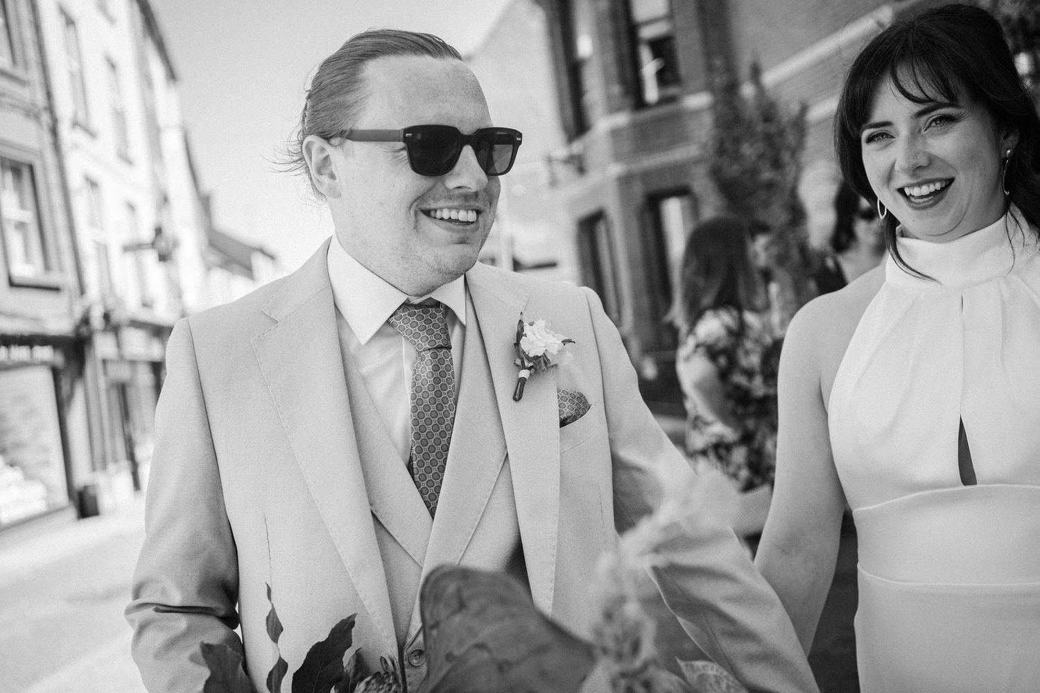 Black and white candid photos from a wedding showing joyful moments between attendees in formal attire outdoors.