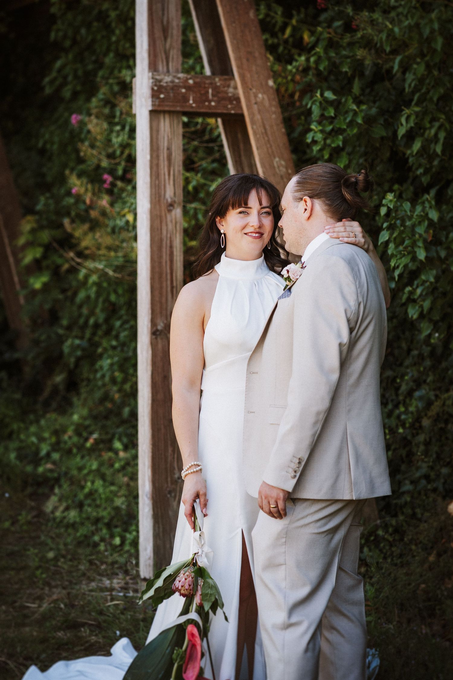 A couple in wedding attire sharing a tender moment together against a leafy green backdrop.