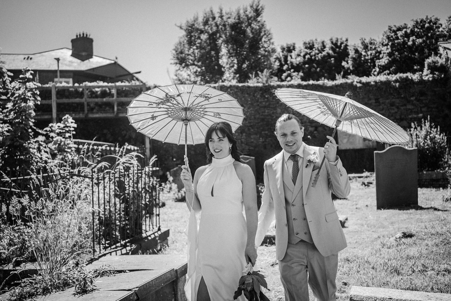 Group carrying white parasols through a sunny garden during a black and white vintage wedding photograph.