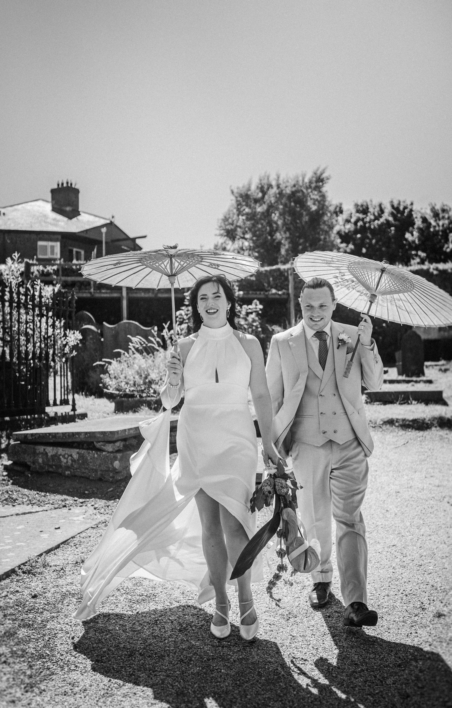 Wedding group walking outside with white parasols creating artistic shadow play in black and white photography.