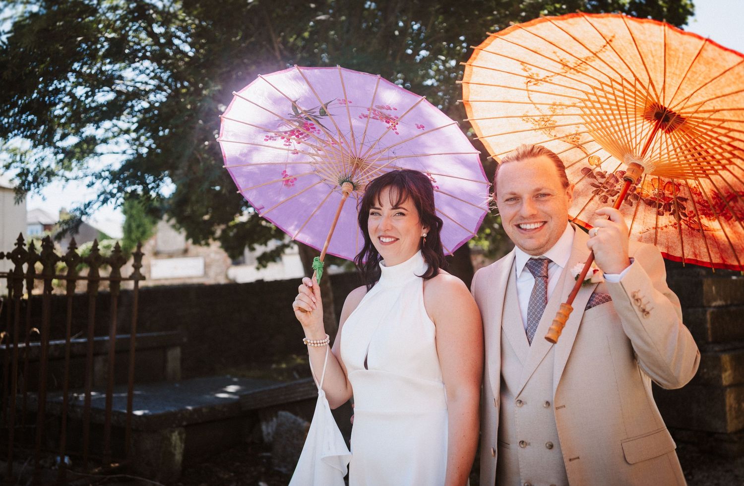 Group holding colorful paper parasols outdoors during sunset celebration at wedding ceremony.