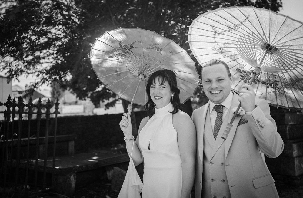 People in black and white pose with decorative umbrellas during an outdoor gathering.