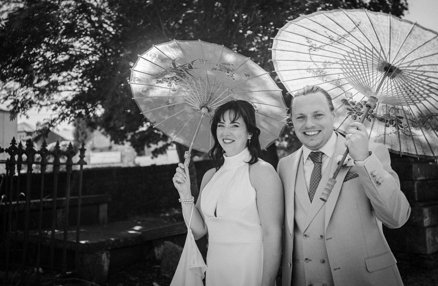 People in black and white pose with decorative umbrellas during an outdoor gathering.