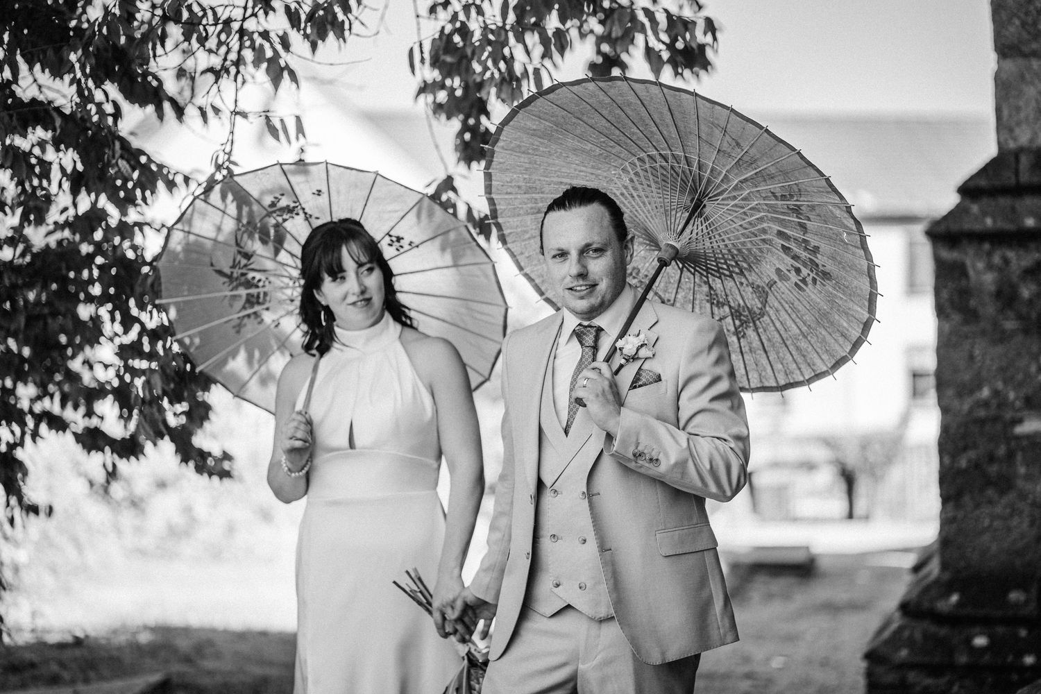 Bridal party holds white parasols as they pose together for a black and white outdoor wedding photograph.