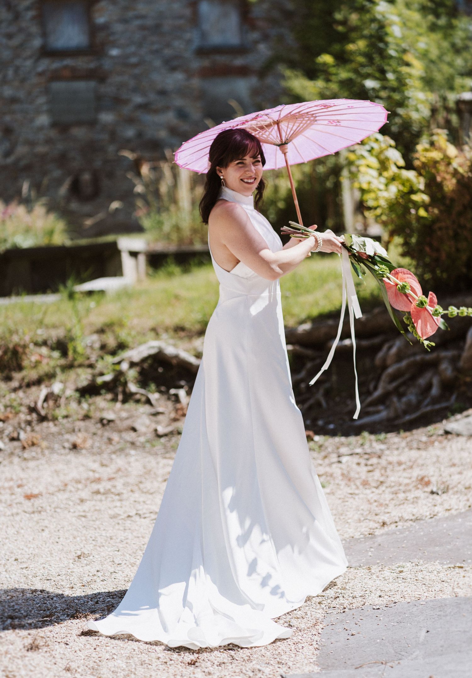 Series of shots capturing someone in a white wedding dress holding a pink parasol against a rustic stone backdrop.