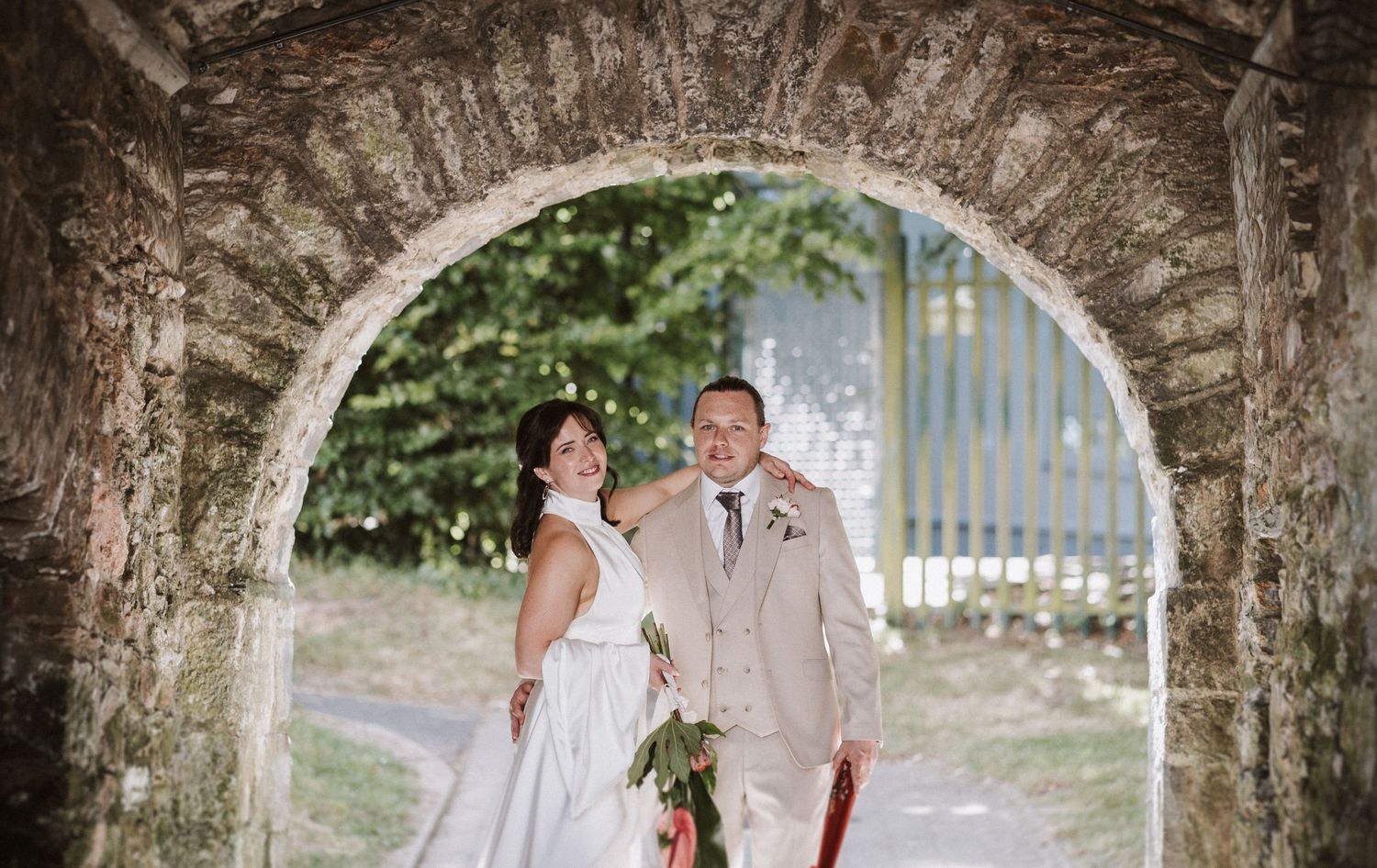 Happy couple sharing tender moments along a tree-lined path during their rustic outdoor wedding celebration.