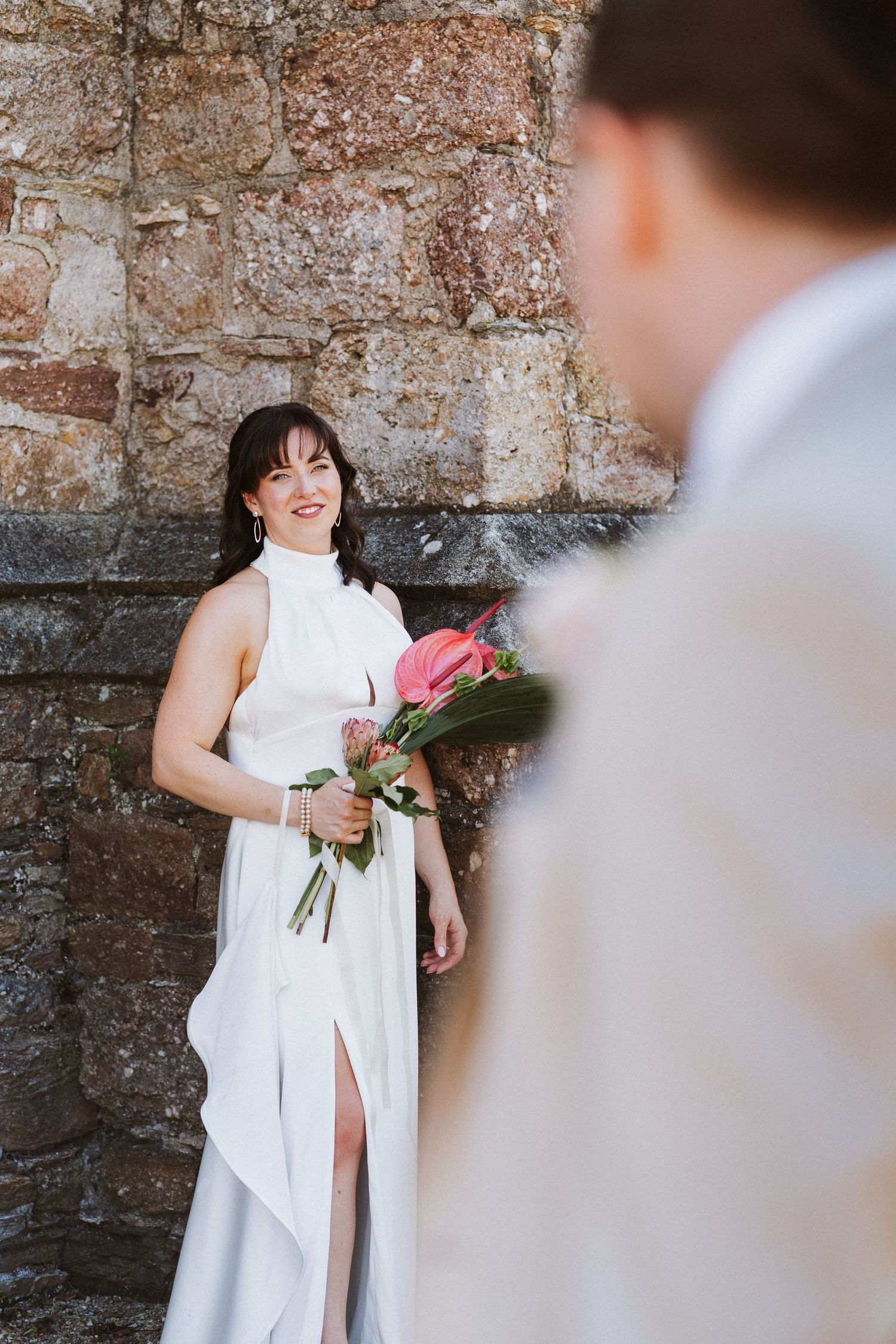 A series of candid moments against a weathered stone wall with someone in an elegant white dress holding flowers.