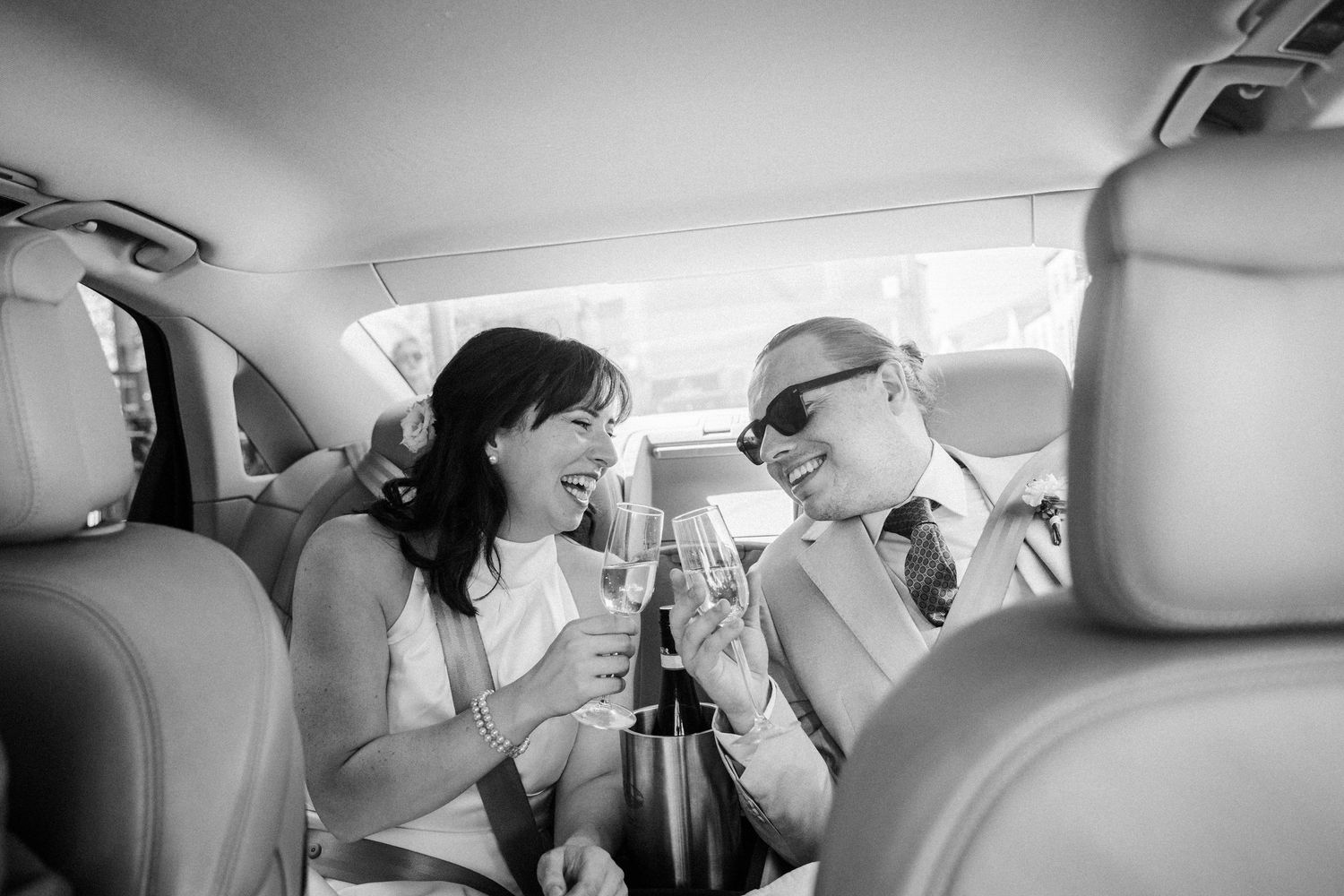 Two people share an intimate moment while seated in the back of a car during what appears to be a rainy day.
