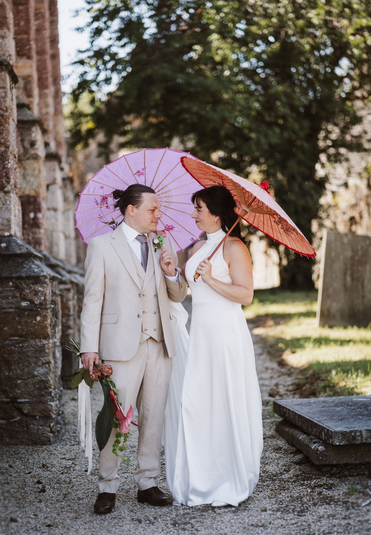 A couple shares romantic moments with parasols while posing in their wedding attire among stone ruins.