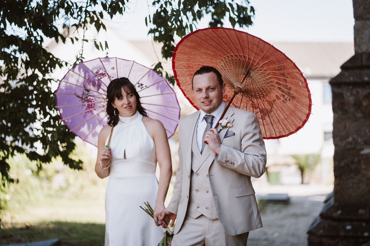 Four wedding photos with couples holding decorative paper parasols, each styled in traditional white formal attire.