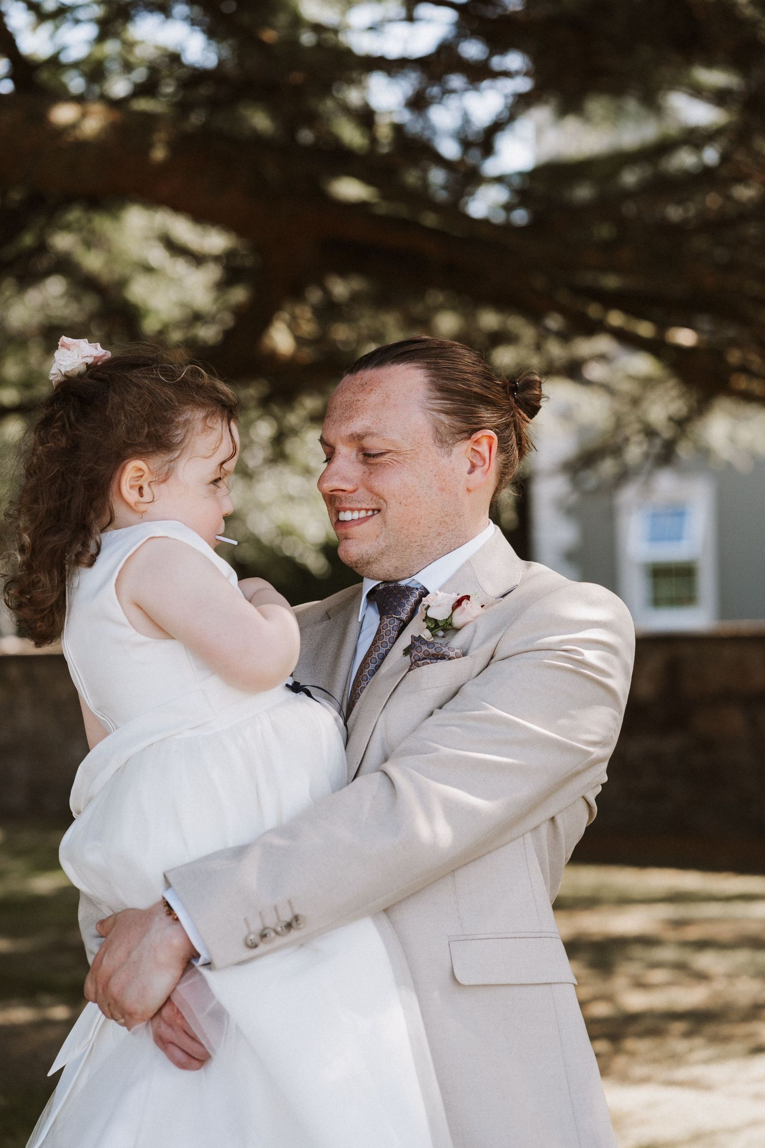 A happy couple in white outfits embraces joyfully during their wedding first look moment outdoors.