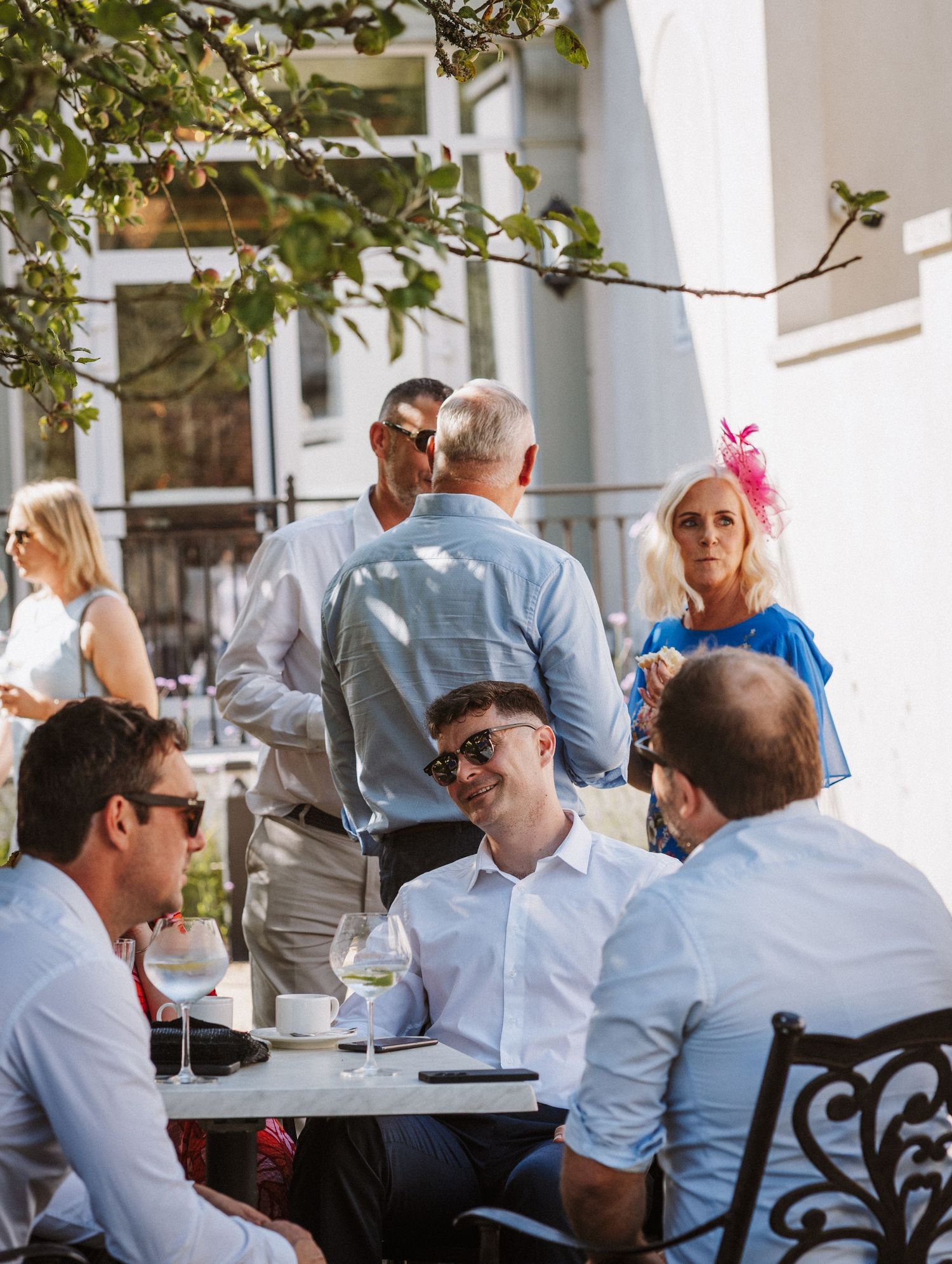 Well-dressed guests mingle and socialize at an outdoor patio restaurant during daytime festivities.