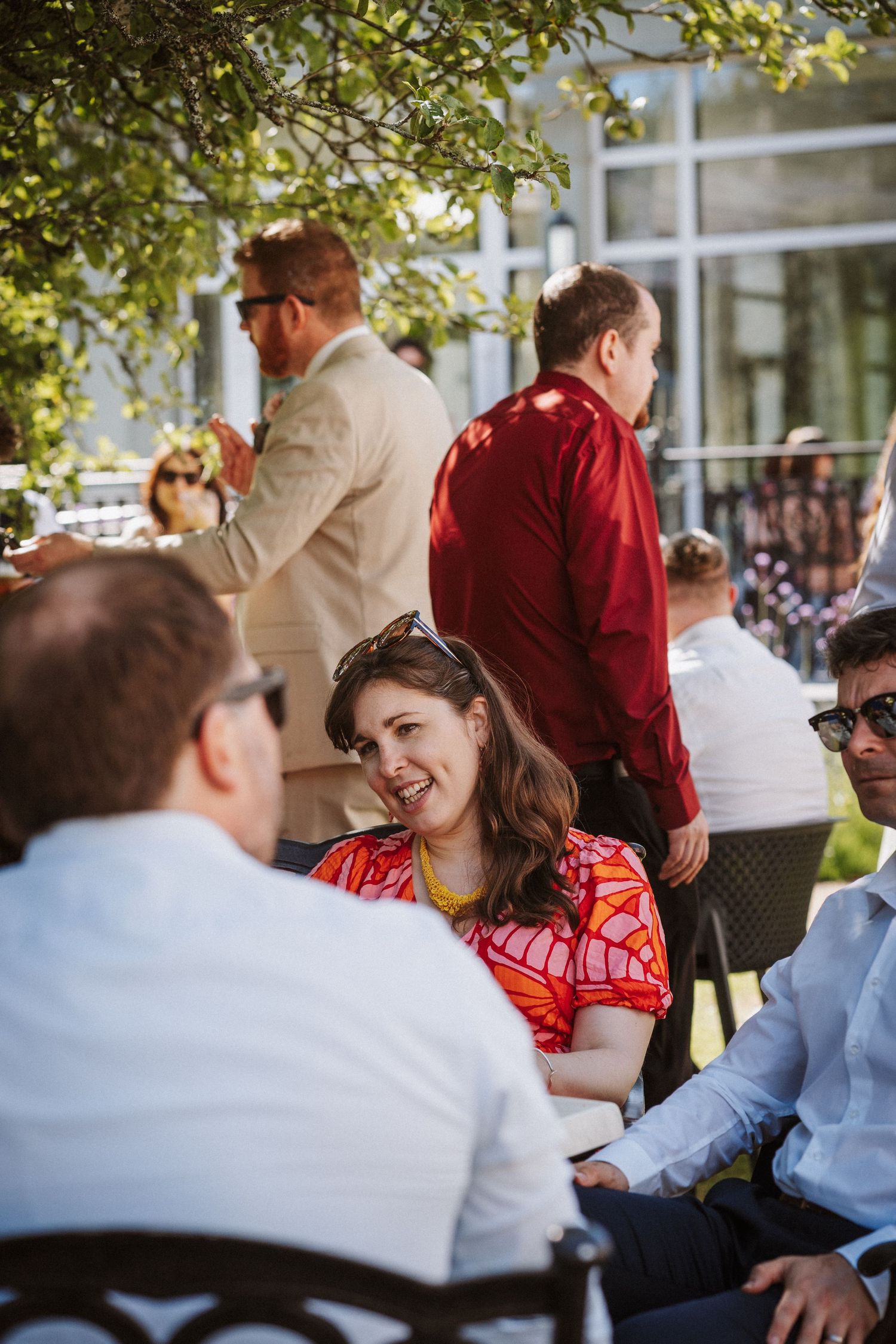 A group of people dining outdoors at a restaurant patio surrounded by green foliage.