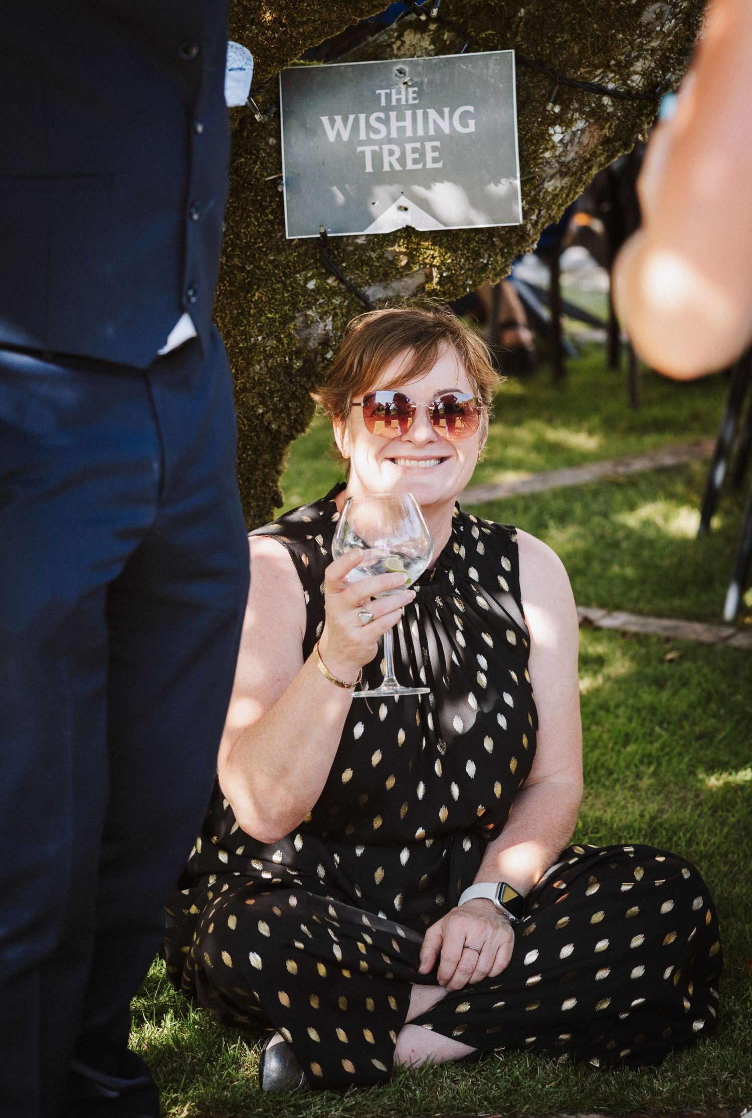 A group of outdoor photos showing someone in a polka dot dress sitting on grass near a sign that reads 'The Wishing Tree'.