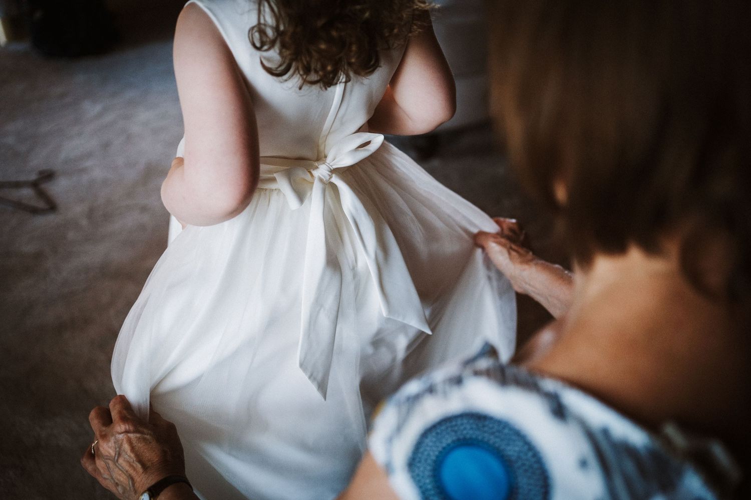 Wedding dress details being adjusted in soft natural lighting.
