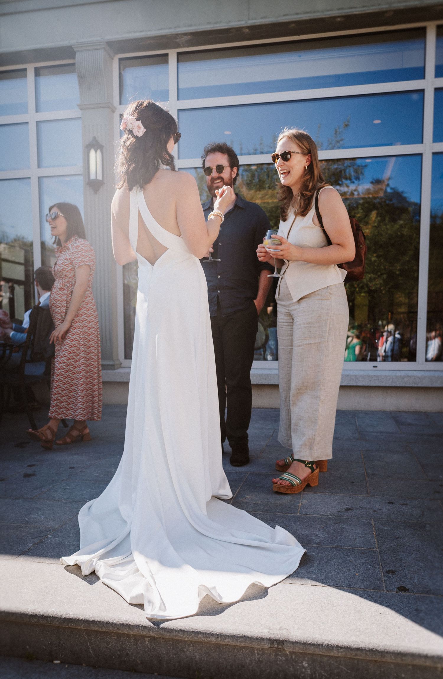 A wedding dress train drapes elegantly across a concrete sidewalk during an outdoor celebration.
