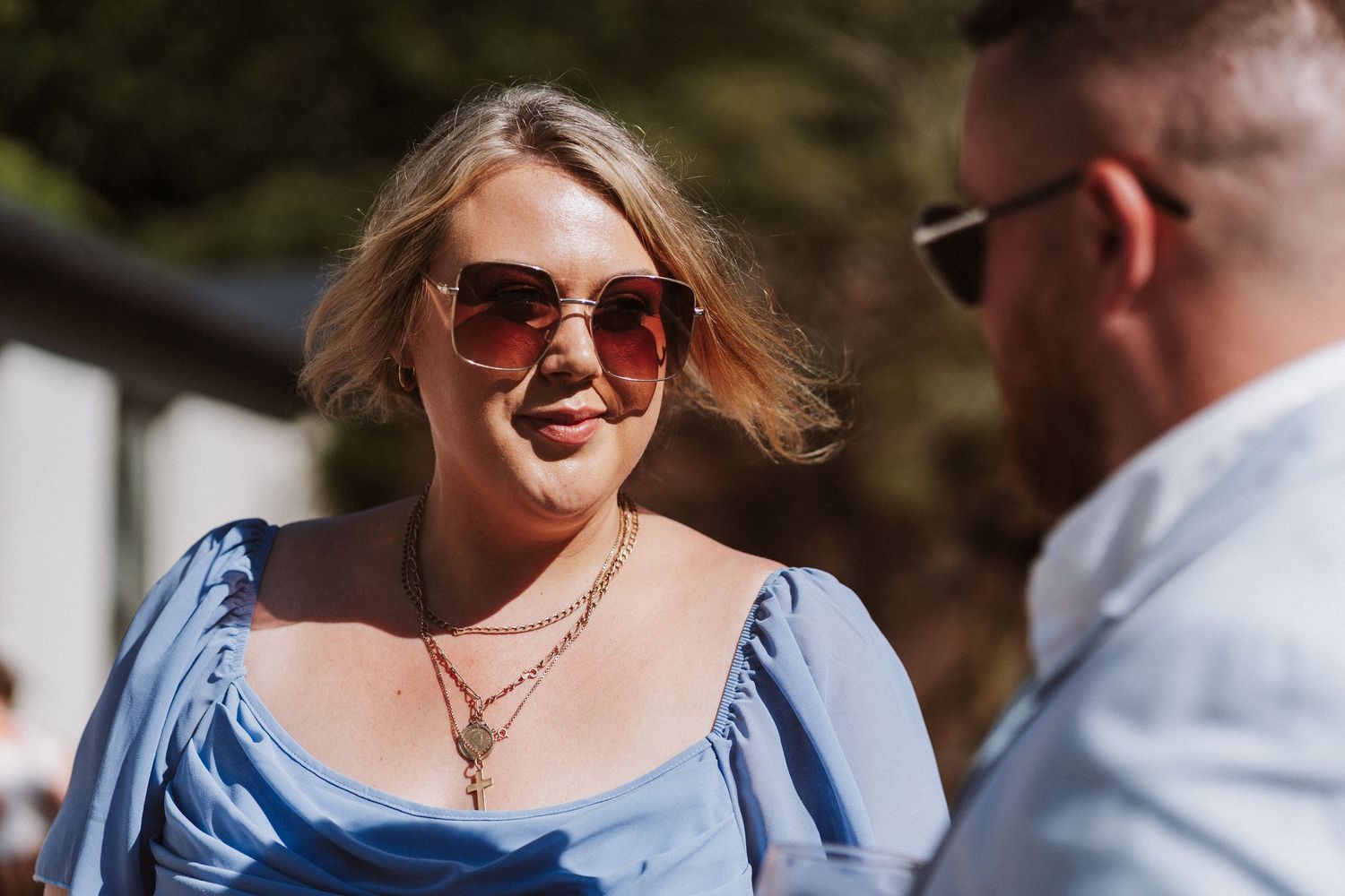 Two people share a candid outdoor moment while smiling and conversing on a sunny day.