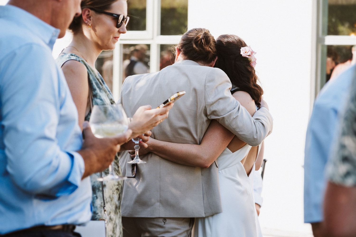 Two people embrace while celebrating at an outdoor event surrounded by guests holding drinks.