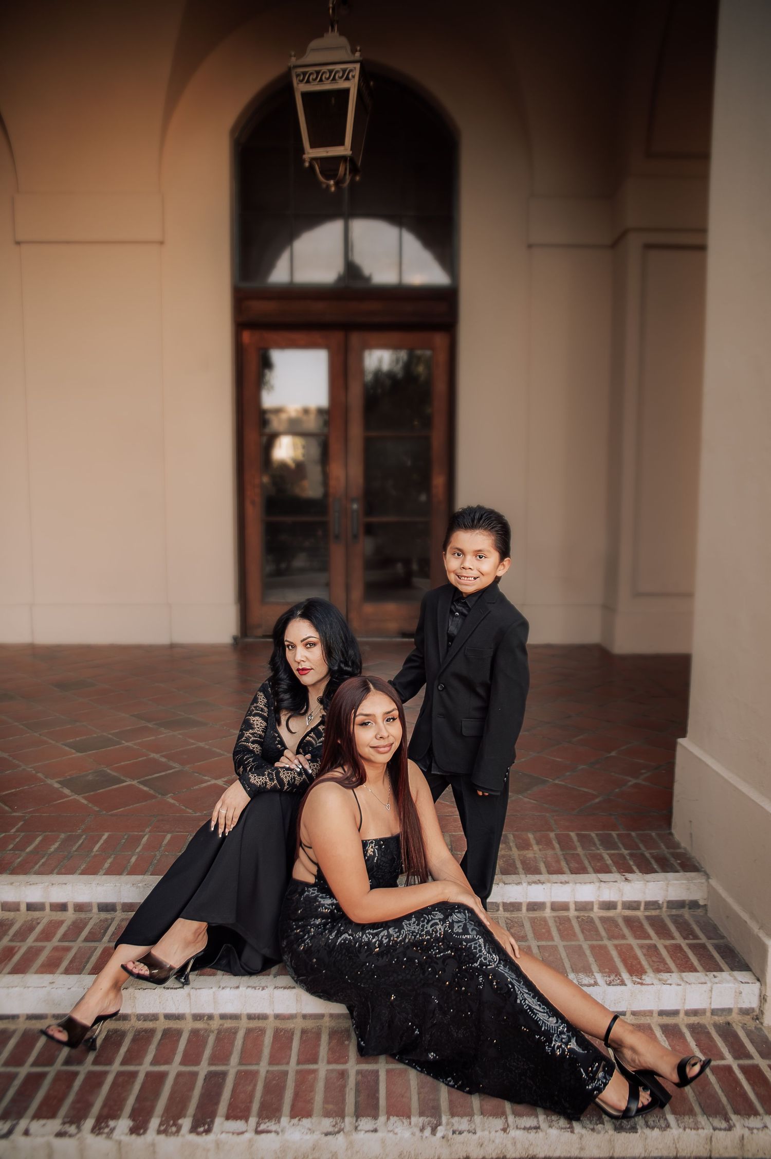Elegant couple poses for romantic formal portraits on a tiled porch, wearing black evening attire.