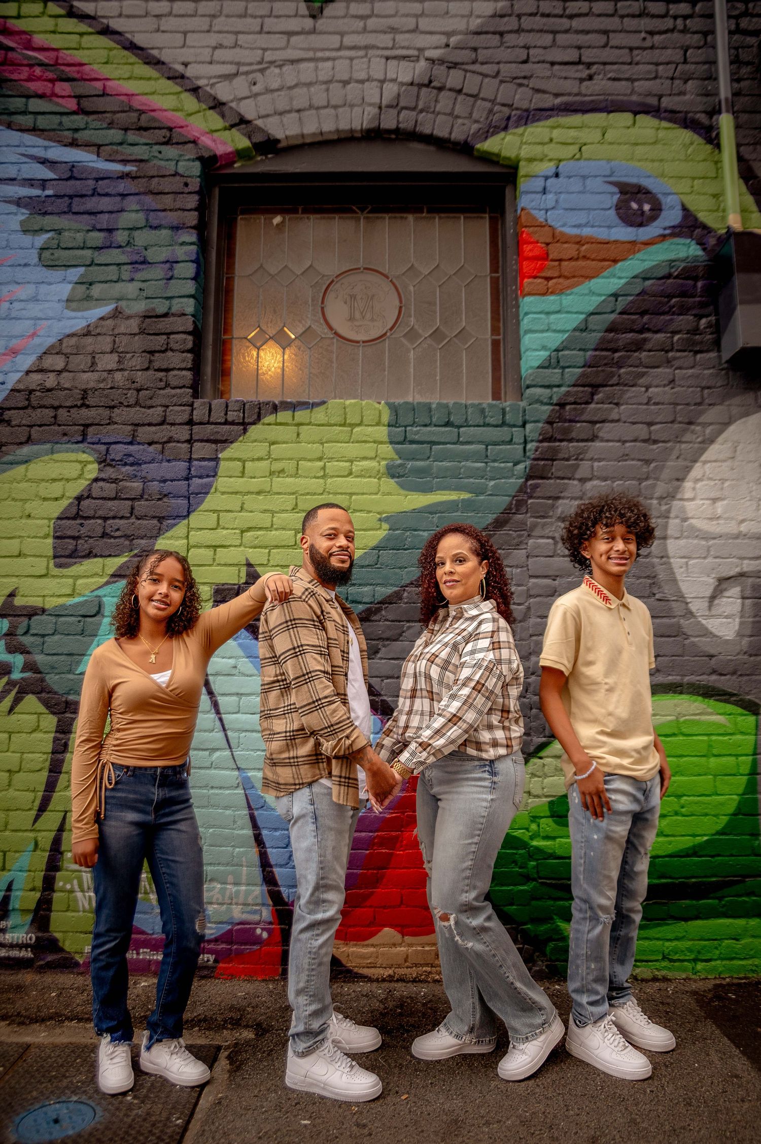Friends posing casually against colorful urban mural wall with playful expressions.