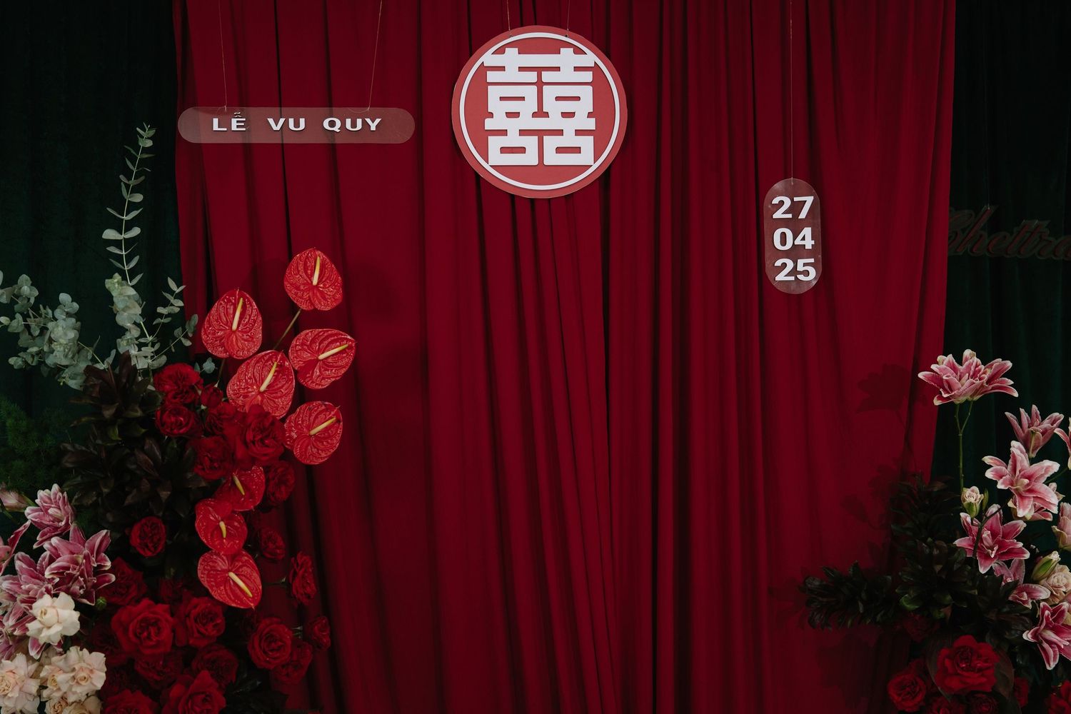 Traditional Chinese wedding backdrop with double happiness symbol, red flowers, and Le Vu Quy signage.