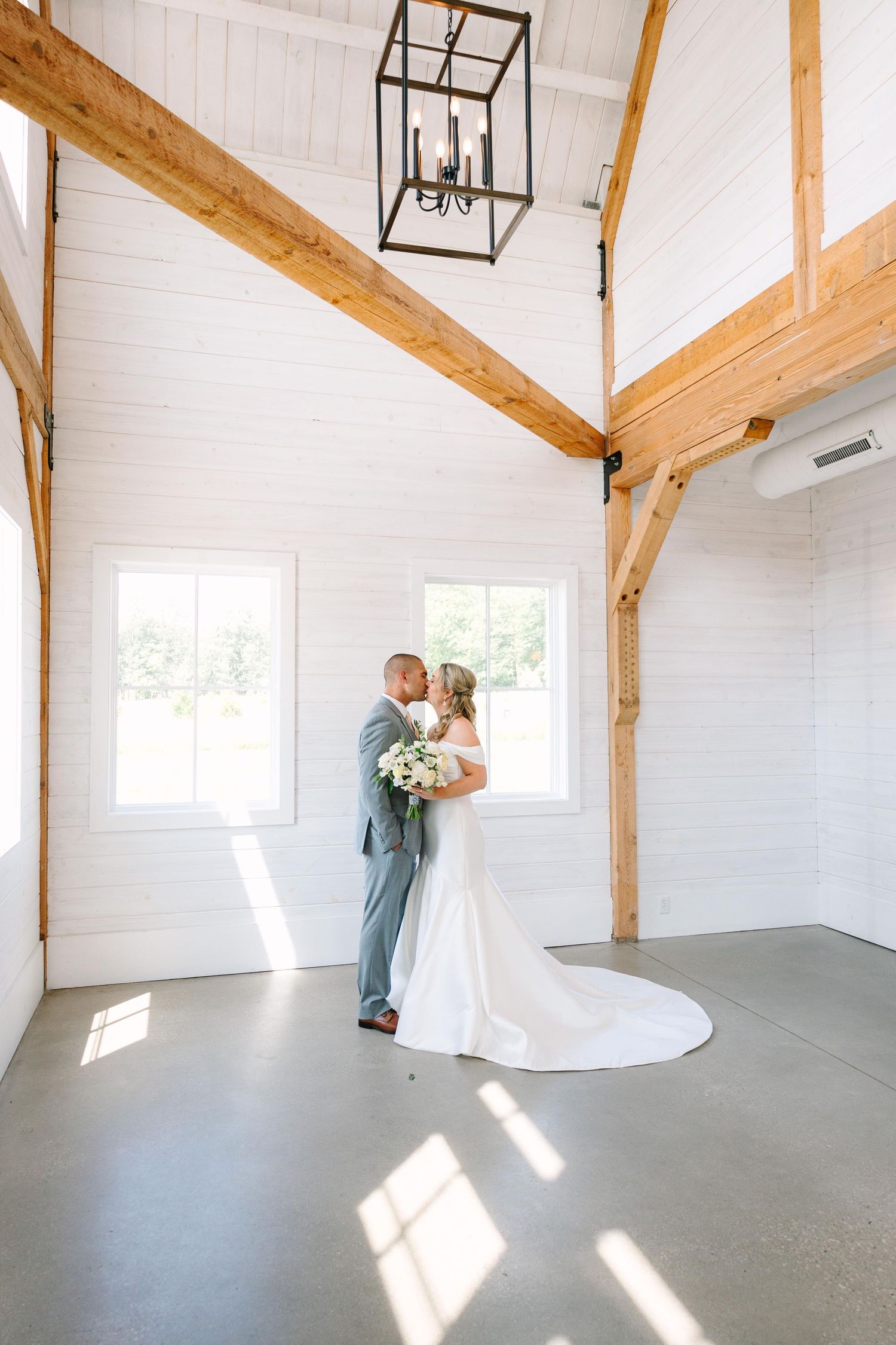 A romantic wedding moment captured under a delicate veil as couple shares tender kiss with white roses in hand.